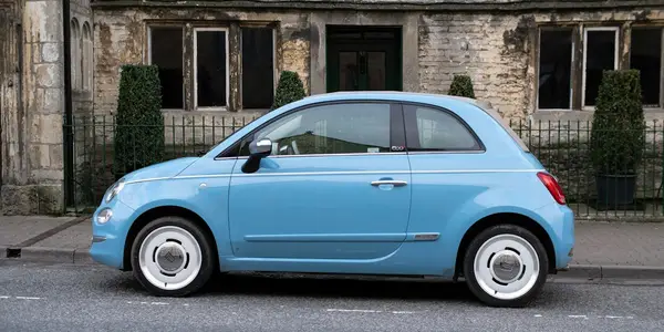 Petite voiture bleue garée devant une maison en pierre